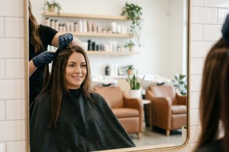 Femme en salon de coiffure recevant la pose d'extensions capillaires par une styliste professionnelle
